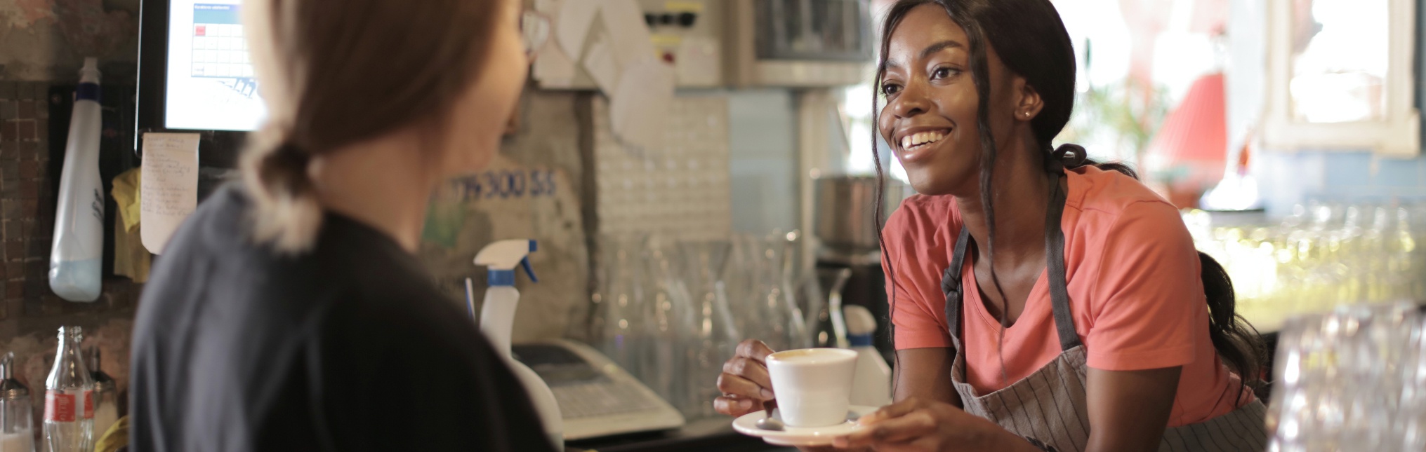Delighted black female barista serving coffee in cup in cafe